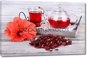 чай из гибискуса в стеклянном чайнике и цветок на цветной салфетки на деревянном фоне
